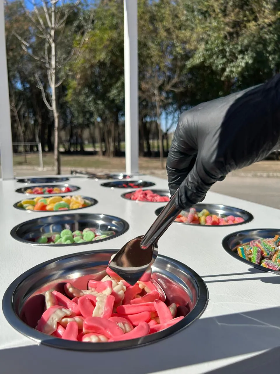 Persona con guantes sirviendo gomitas con pinza desde los bowls de acero